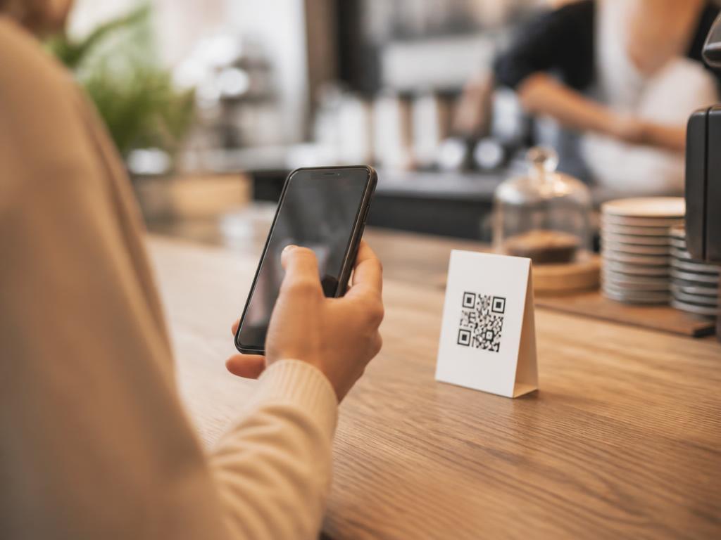 Une cliente scanne le QR code Touia au comptoir d'un café avec son téléphone